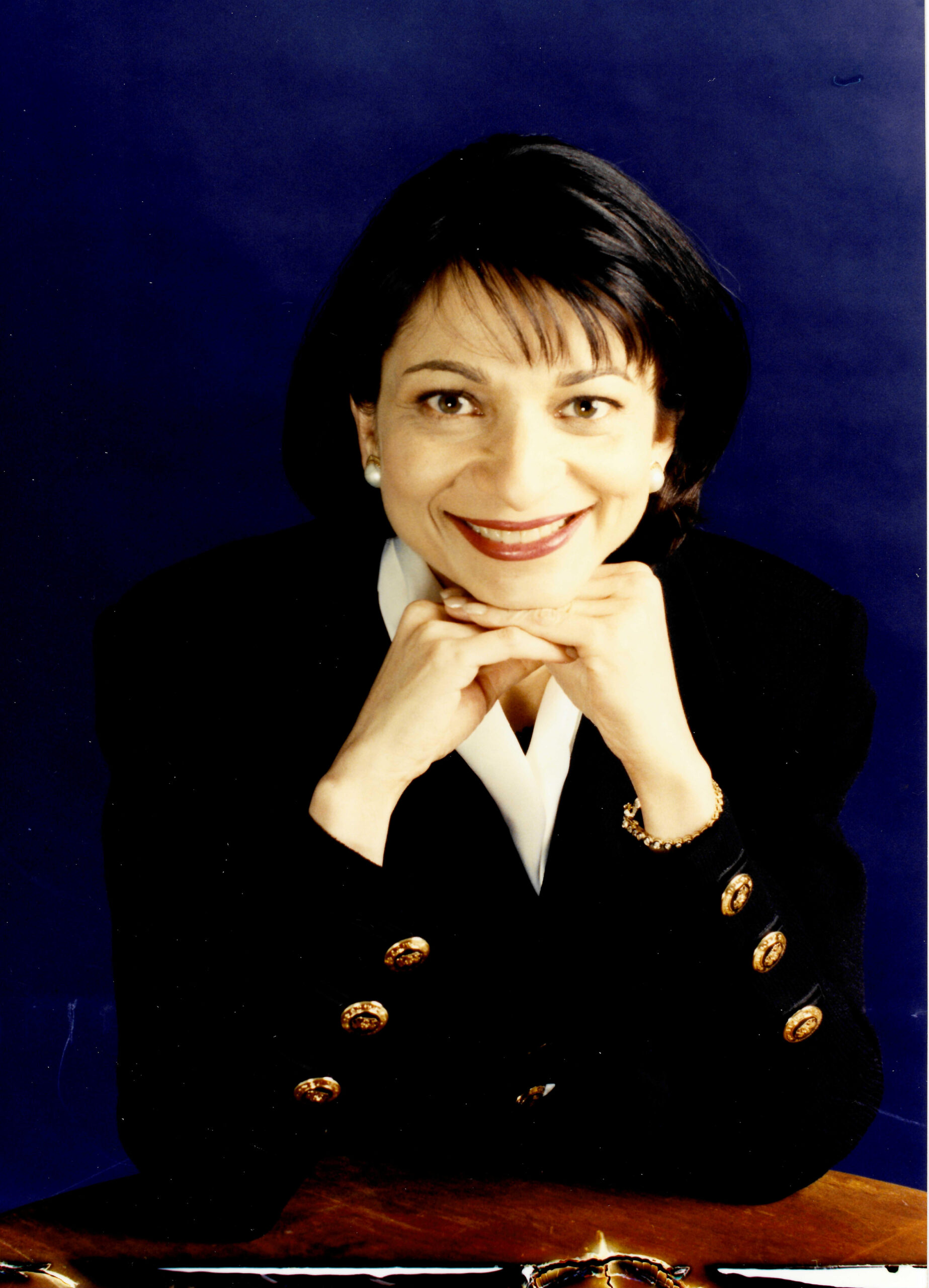 Anu Saad headshot wearing a black blazer with gold buttons